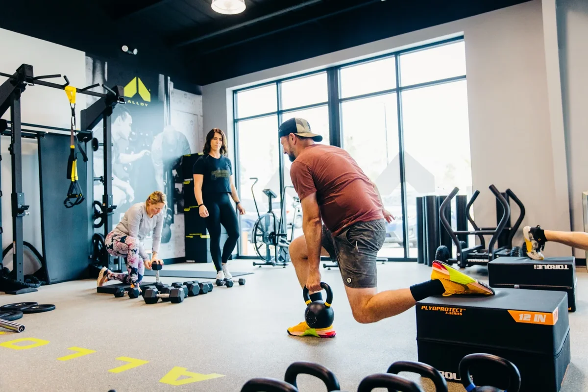 A small group of members trains together with coaches on the floor at an Alloy Personal Training studio