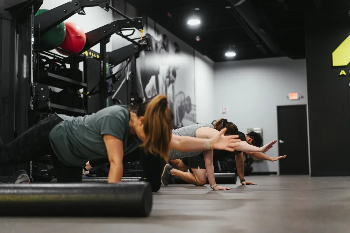 A member holds a plank while reaching forward over a foam roller at an Alloy Personal Training studio