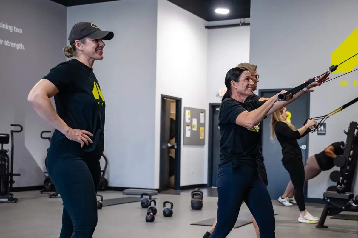A coach cues a member's posture during a standing press exercise at an Alloy Personal Training studio