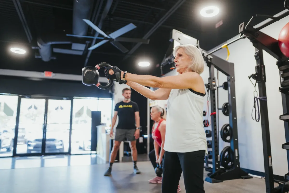 A woman in her 70s works through kettlebell swings during a coached session at an Alloy Personal Training studio