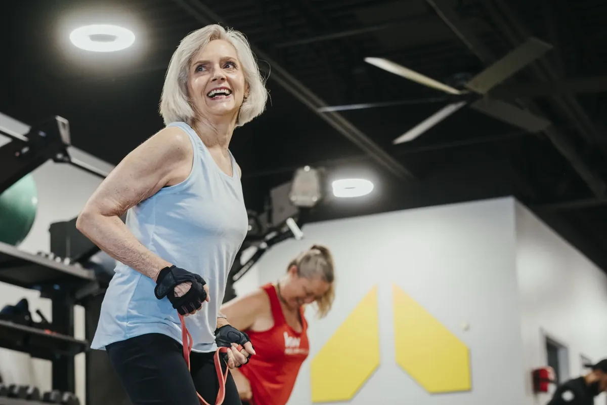 A smiling member works with a resistance band during a relaxed small group session at an Alloy Personal Training studio
